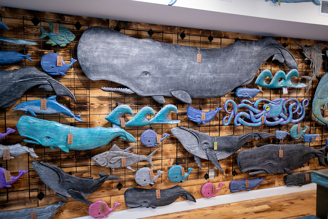 About a dozen wooden carved sea creatures painted blues and greens hang on display in a store